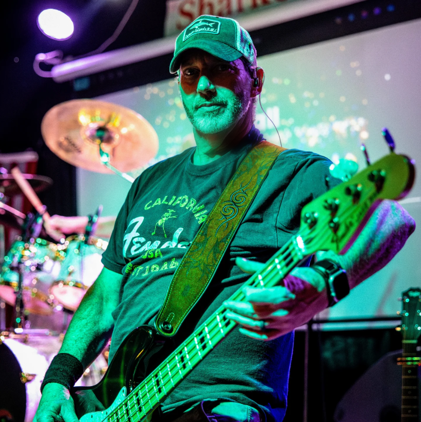 Jason G. performing live on bass, stage lit in green and violet